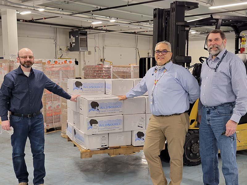 three men standing by a pallet with boxes on it