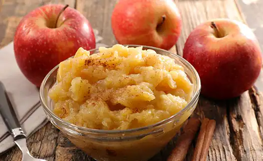 bowl of applesauce with whole apples behind it