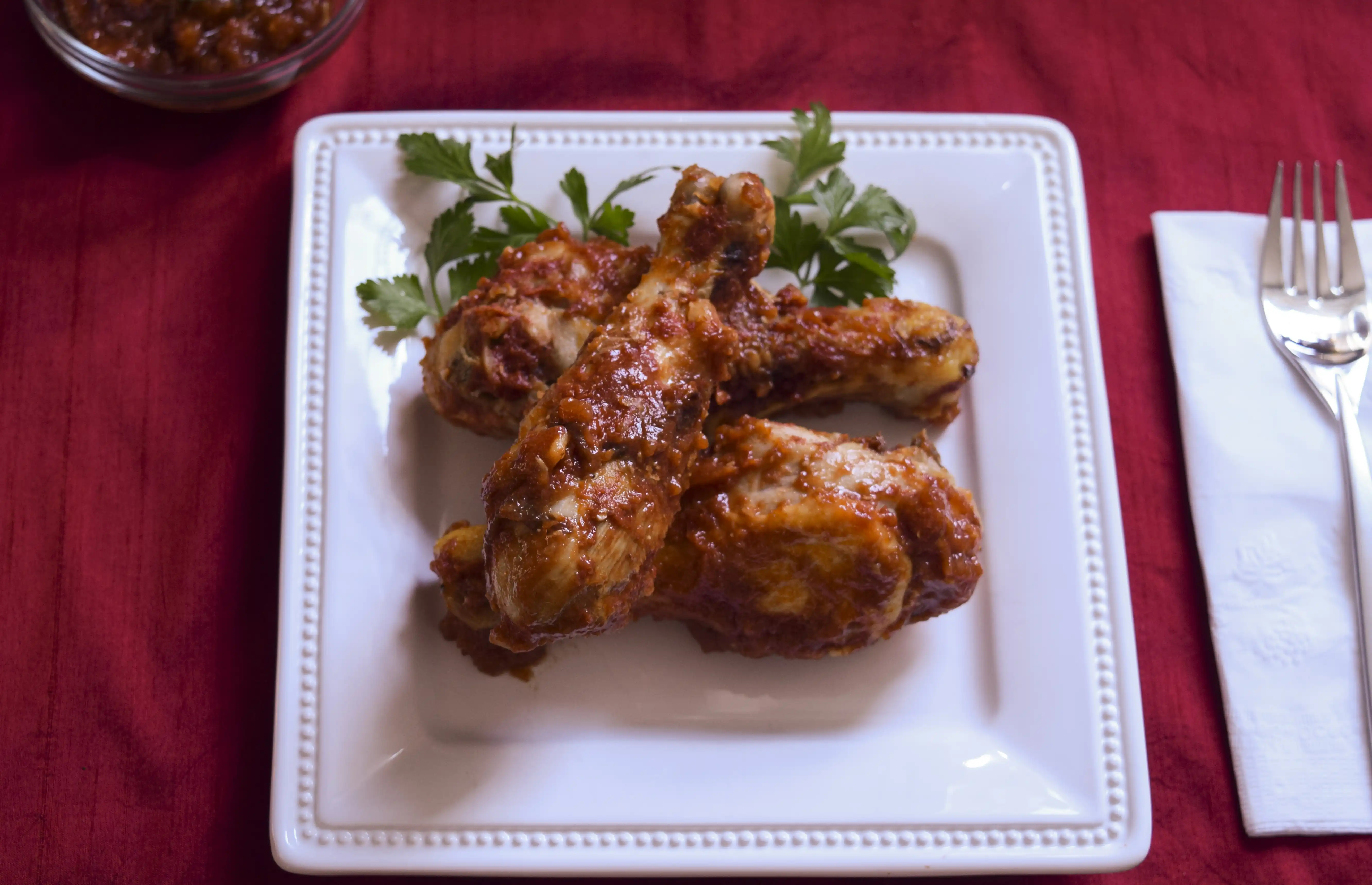 barbecue chicken on a white plate sitting on a red tablecloth