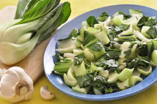 a plate with garlic bok choy and a whole bok choy and garlic head on the side