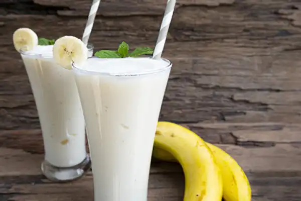 two glasses of iced milk shakes with a banana on the side