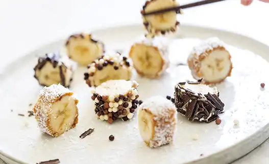 white plate with bananas covered in peanut butter and chocolate