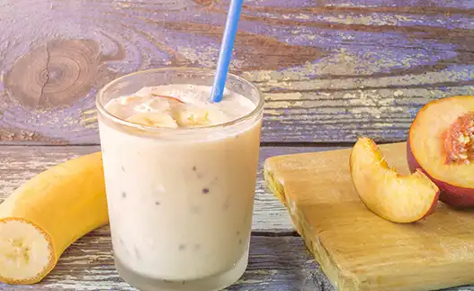 peach smoothie with a straw and sliced peaches on the side