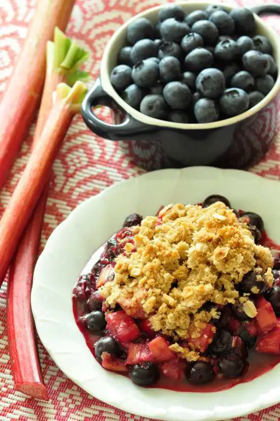 plate of rhubarb blueberry crisp with a bowl of blueberries on the side