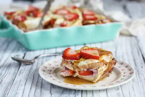 a baking dish with a piece removed on a plate of strawberry french toast casserole