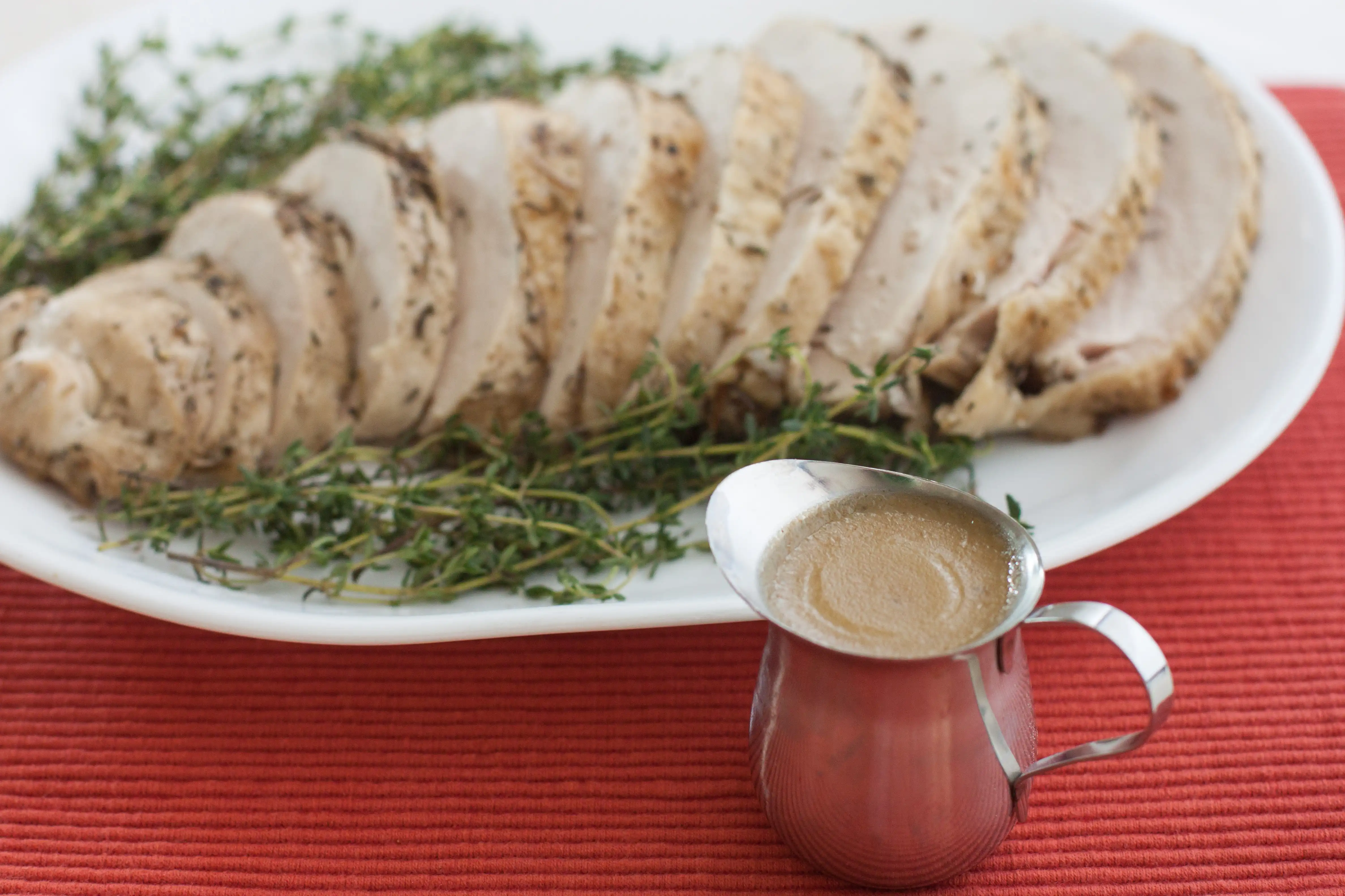 pitcher of gravy next to a plate of sliced turkey