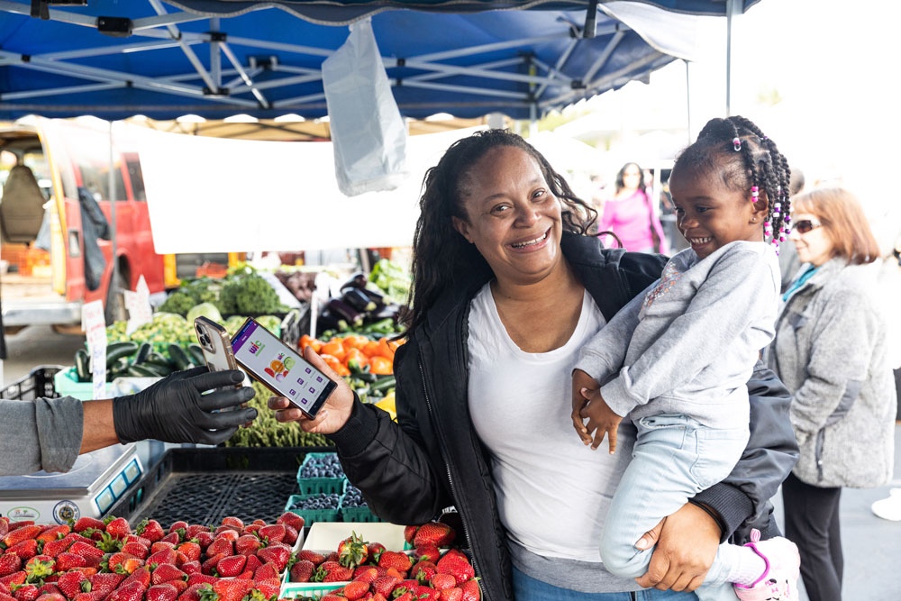 mom using wic at a farmer's market holding her daughter