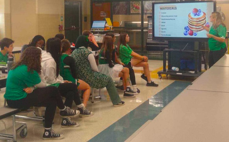 students in a school cafeteria watching a presentation