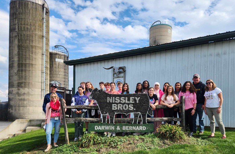 Cooking club students visit Nissley Brother Farms and pose for a group photo in front of the farm sign.