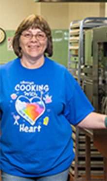 woman working in a school cafeteria opening an oven 