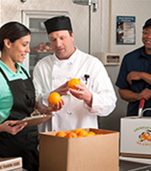 two school meal professional inspecting a delivery of oranges