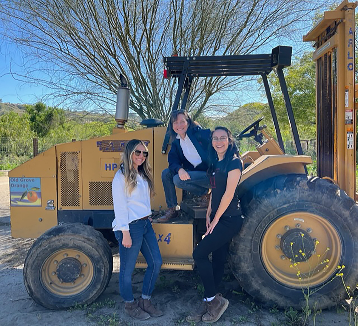 Three women standing next to a tractor.