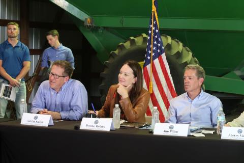 Secretary Rollins at a table listening to farmers with the American flag behind her.