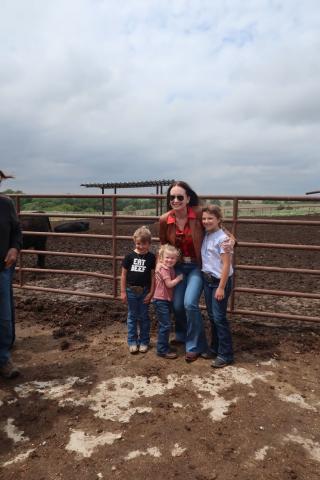 Secretary Rollins with 3 children posing in front of a cattle gate.