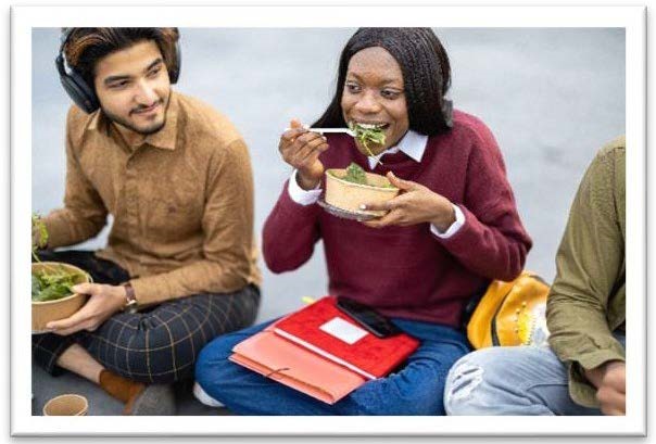 college students sitting on the ground eating salad with notebooks in their laps