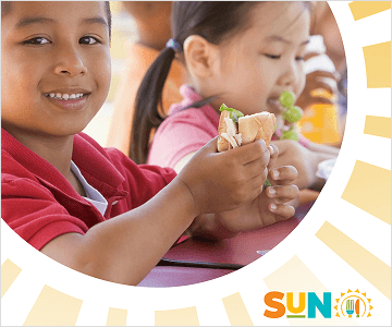 image of a littel boy holding a sandwich and a little girl behind him, with sunrays and the sun logo