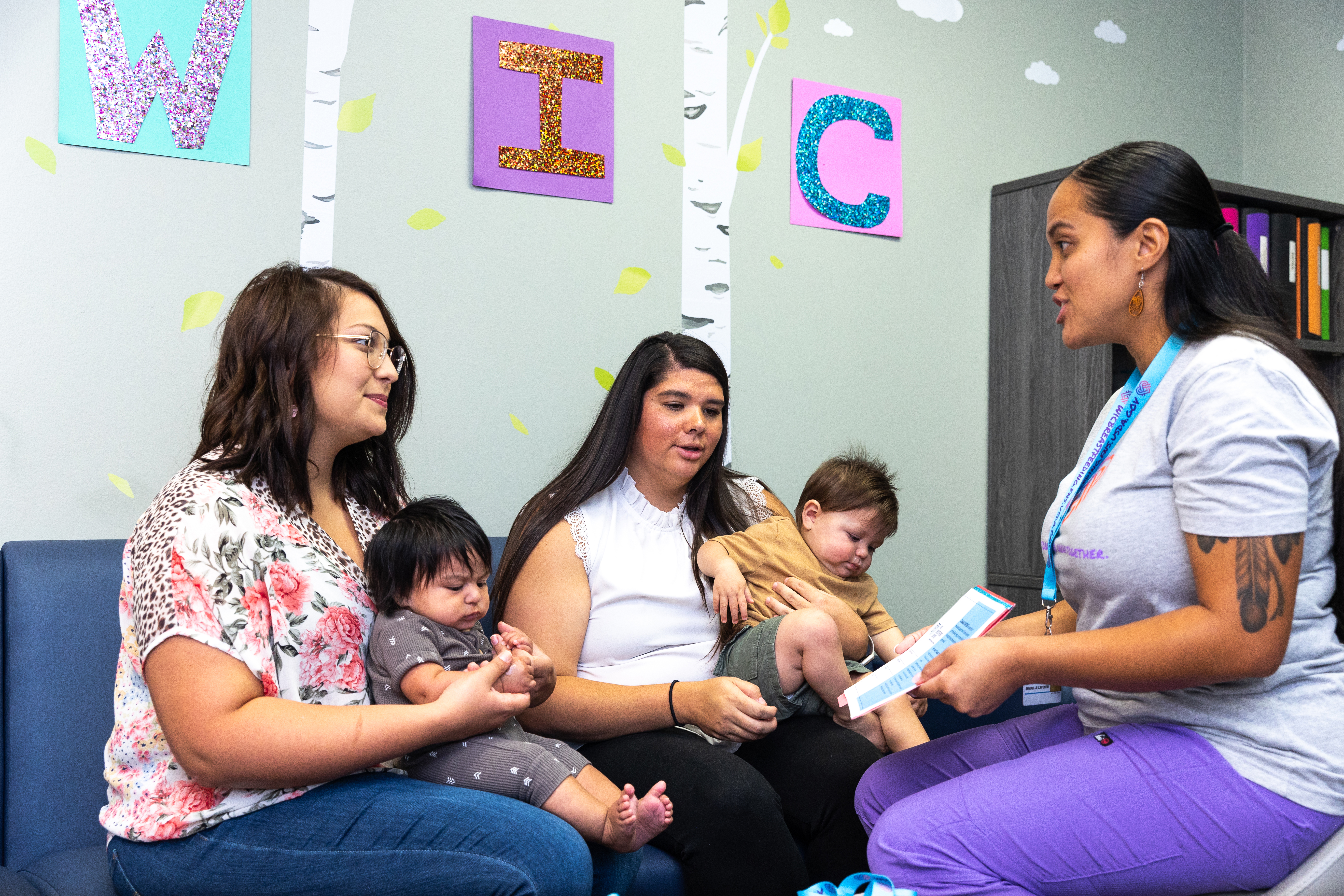 A WIC staff member talking to two women holding infants.