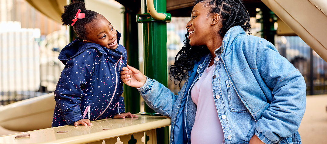 pregnant woman and her daughter smiling at each other on the playground
