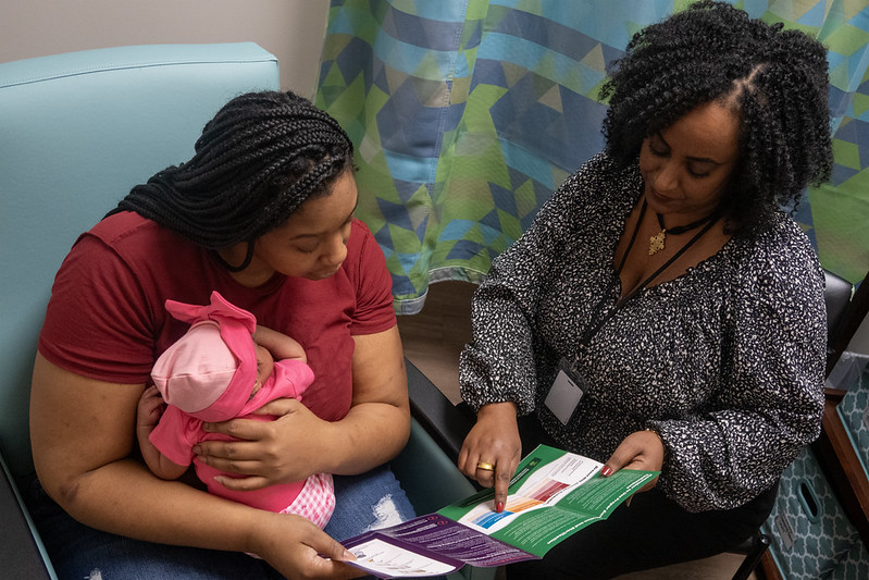 a woman holding an infant looking at a folder with a WIC staff person