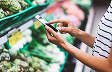 woman holding her cell phone in the produce aisle of a grocery store