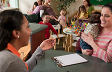 woman holding an infant talking to a woman in a WIC clinic at a table