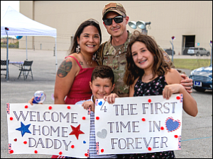 picture of military father coming home to wife and kids with welcome posters