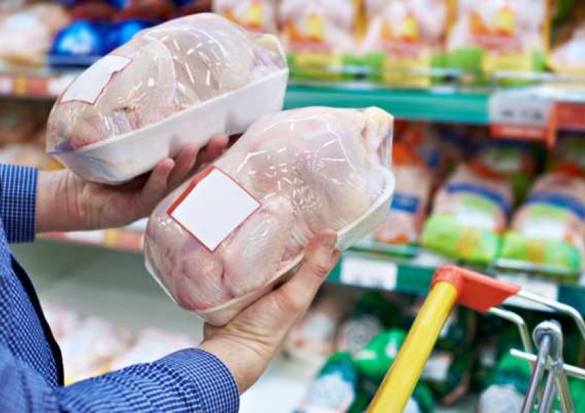 person holding two raw chickens in a grocery store aisle