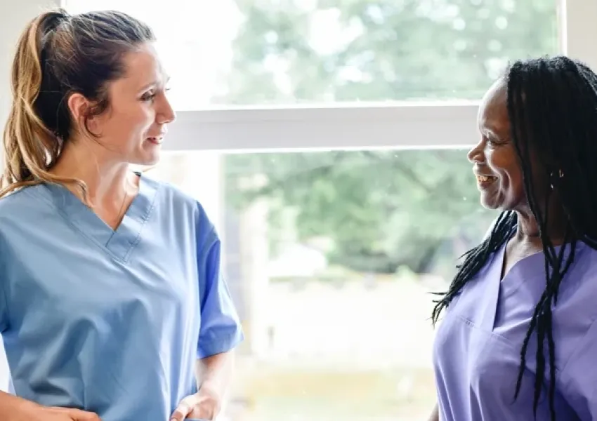 two women wearing scrubs standing in front of a window