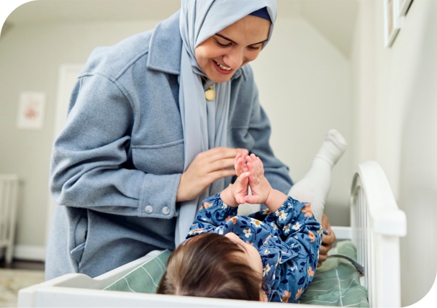 woman wearing a hijab changing a baby's diaper on a changing table