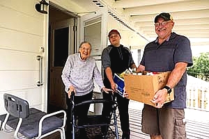 photo of two men deliving food to an older woman using a walker on her porch, all are smiling