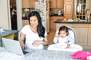 pregnant mom on computer while toddler eats