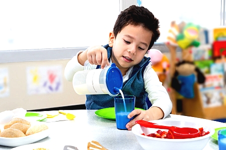 Boy pouring milk family style meal service at child care