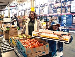 women volunteering at a food bank lifting pallets of tomatoes
