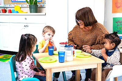 teacher sitting at a table with three small children eating lunch
