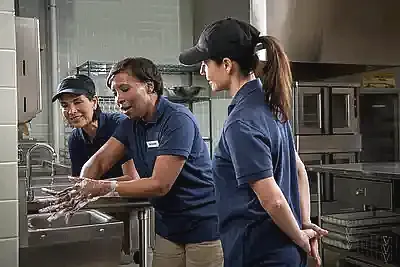 a woman demonstrating proper handwashing technique to two other school nutrition staff