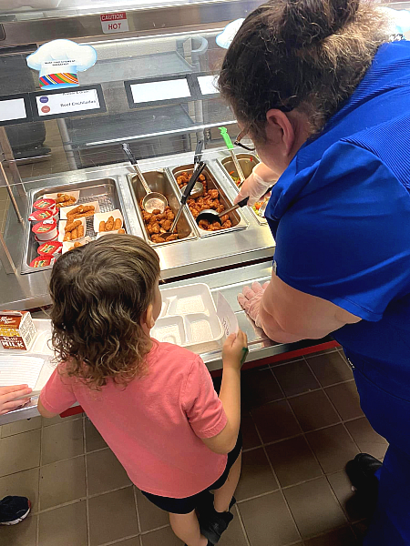 school nutrition professional helping to serve a child in front of a cafeteria line